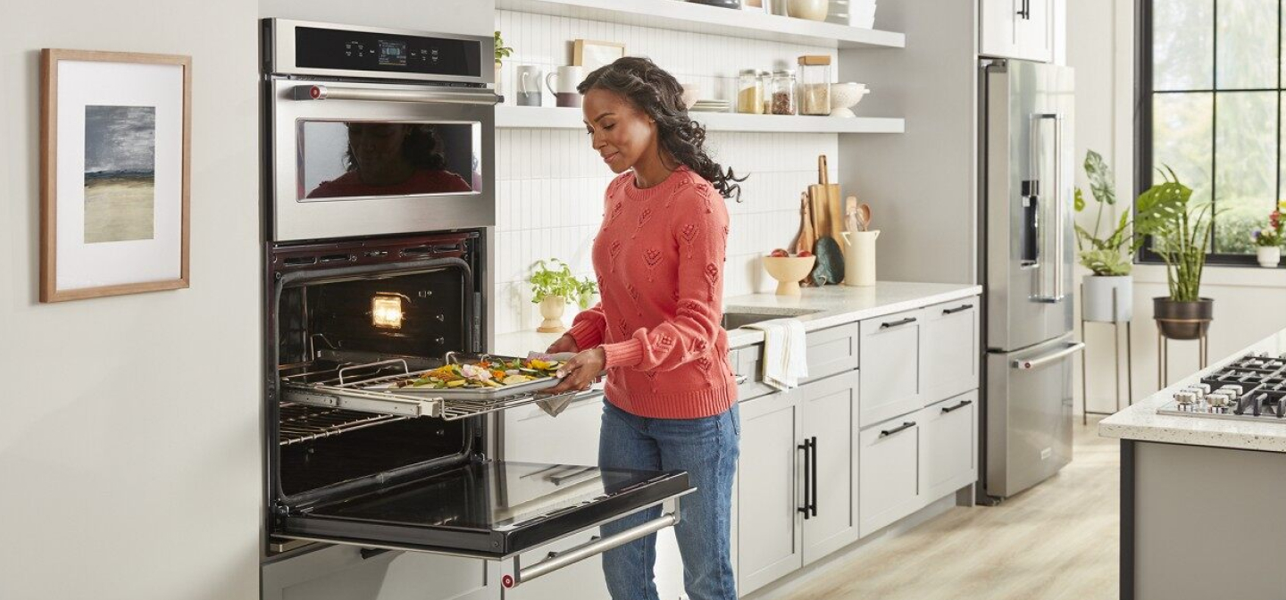 A woman pulling a dish of baked vegetables out of a combination wall oven A woman pulling a dish of baked vegetables out of a combination wall oven